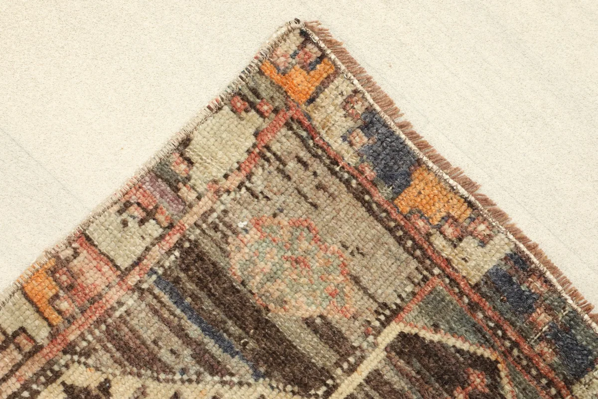 Close-up of a corner showing the hand-knotted texture and muted colors of the border.