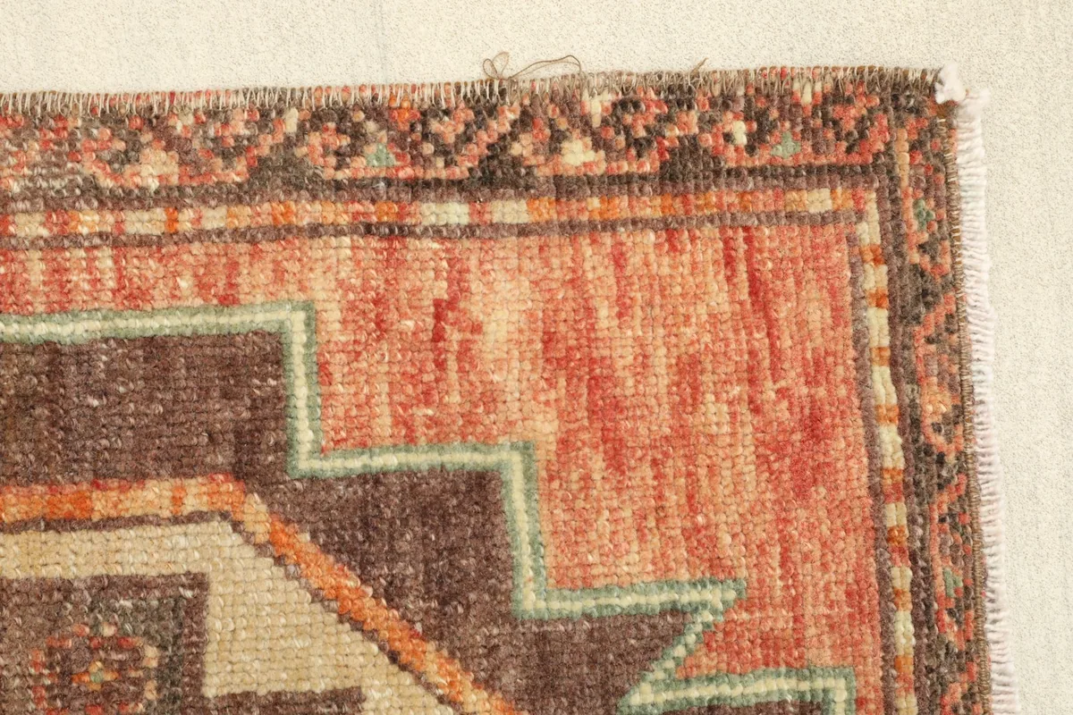 Detail of the rug's edge, revealing the subtle variations in the rust color and the pattern work.
