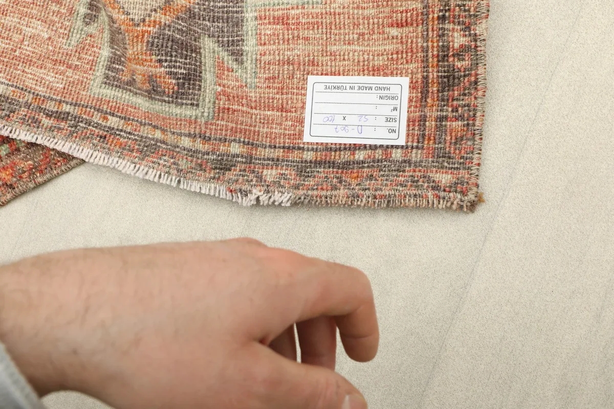 Close-up of the back of the rug with a hand visible, showing the cotton foundation and knotting.
