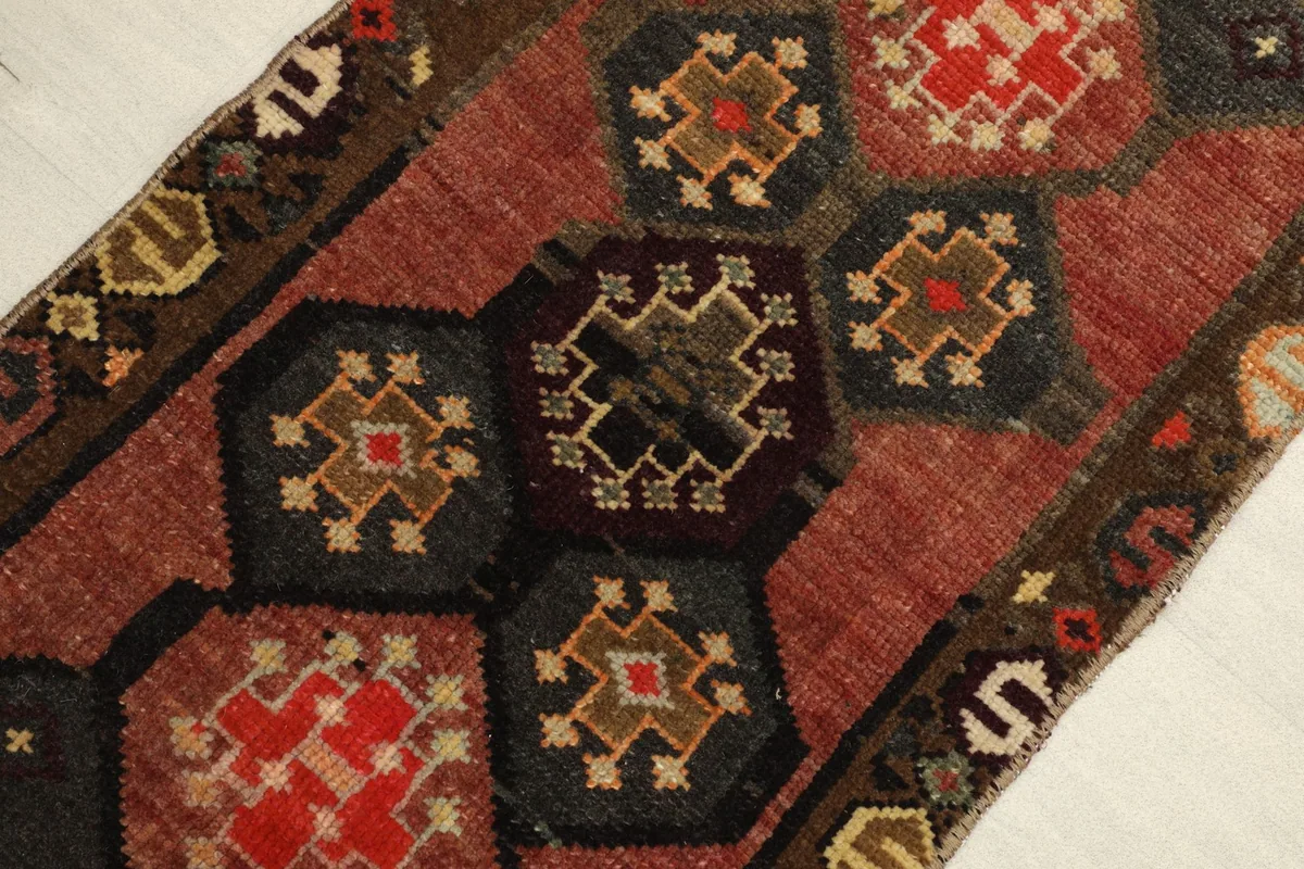 Close-up detail of the central geometric medallions in rust, charcoal, and brown with red and gold accents.