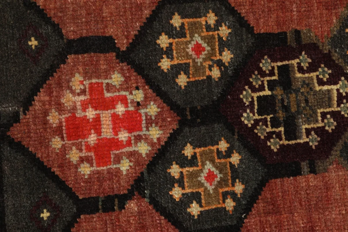 Detailed view of the hand-knotted wool pile, showing the red, charcoal, and brown geometric motifs.
