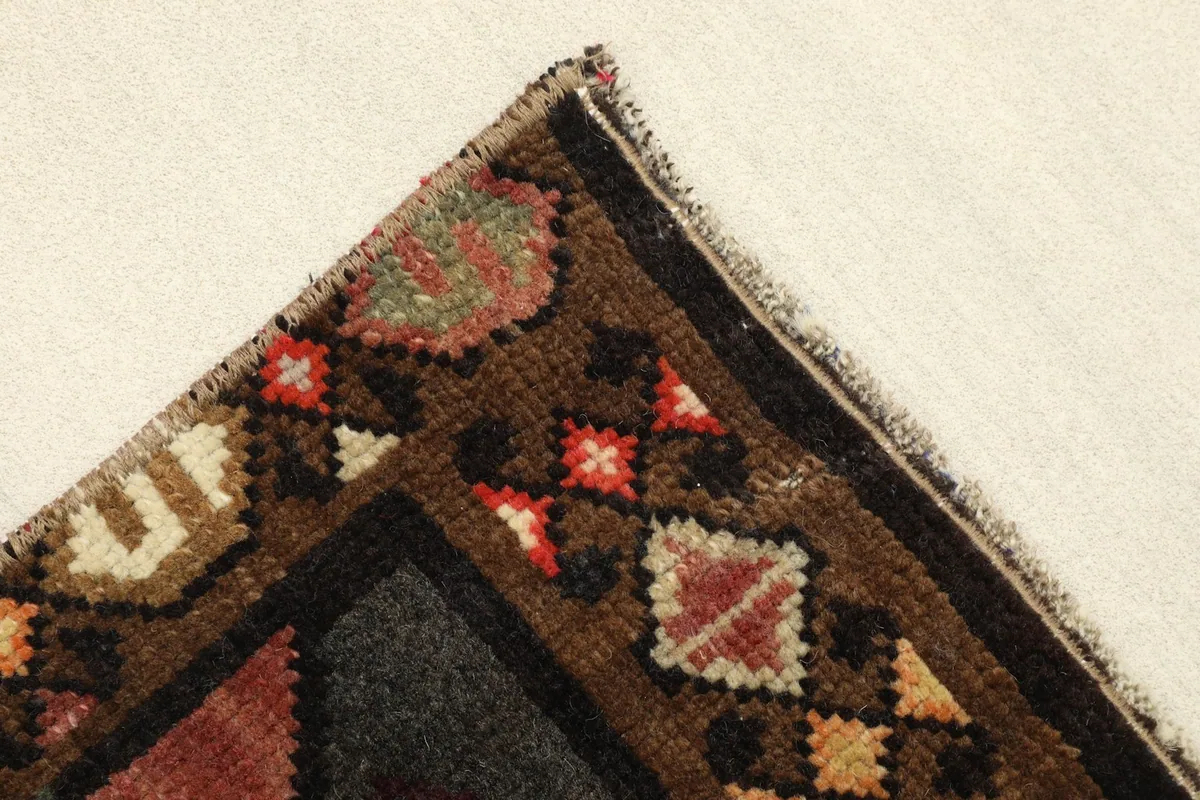Corner detail of the rug, highlighting the brown border with small tribal motifs in various colors.