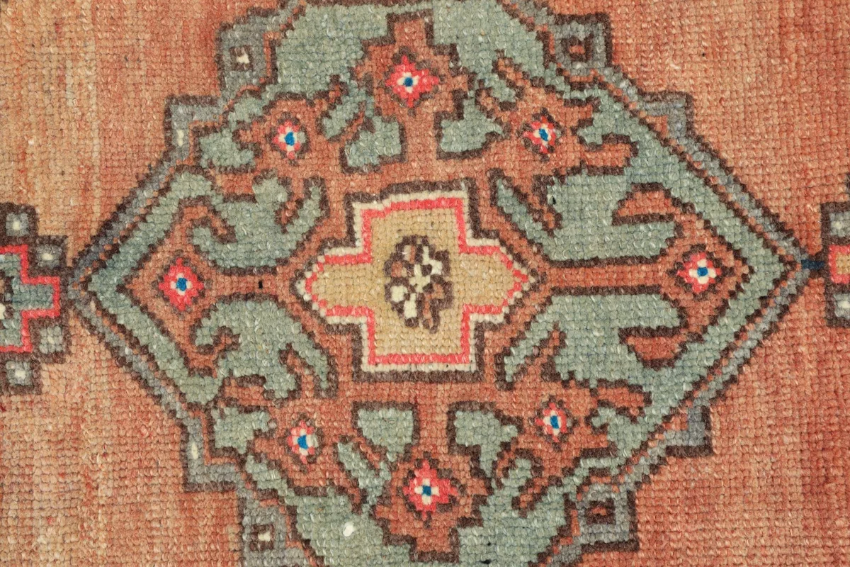 Macro detail of the hand-knotted wool pile, showing the intricate blue, rust, and beige colors of the medallion.