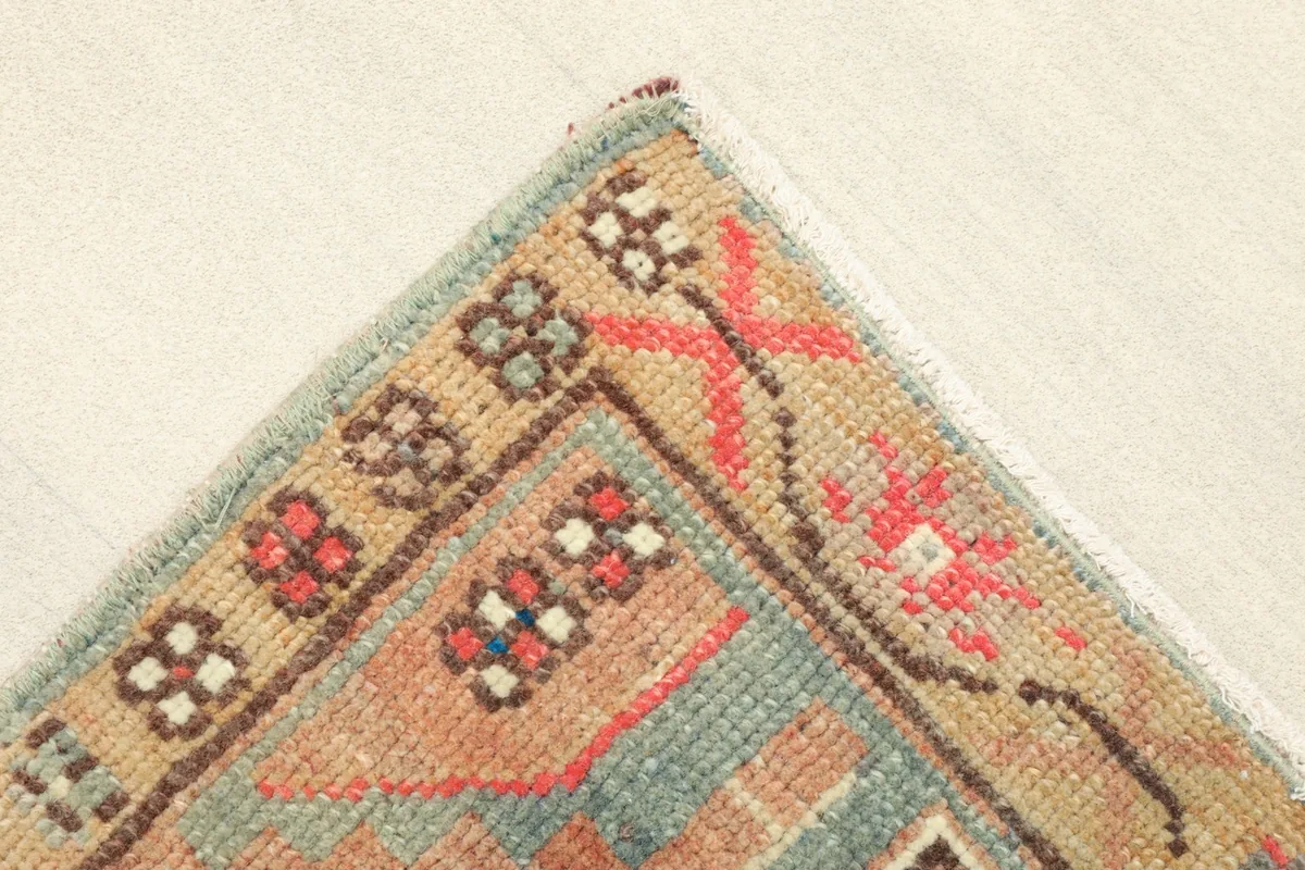 Corner detail showing the beige border with small red and brown motifs, and the light blue edge.