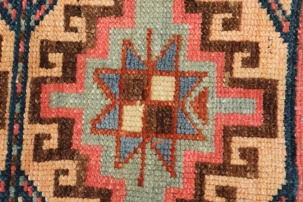 Close-up detail of a central geometric star motif with squares in beige, brown, and blue within the green.