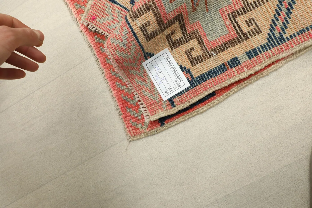 Hand holding the rug to show the woven back and a small tag, indicating its hand-knotted origin.