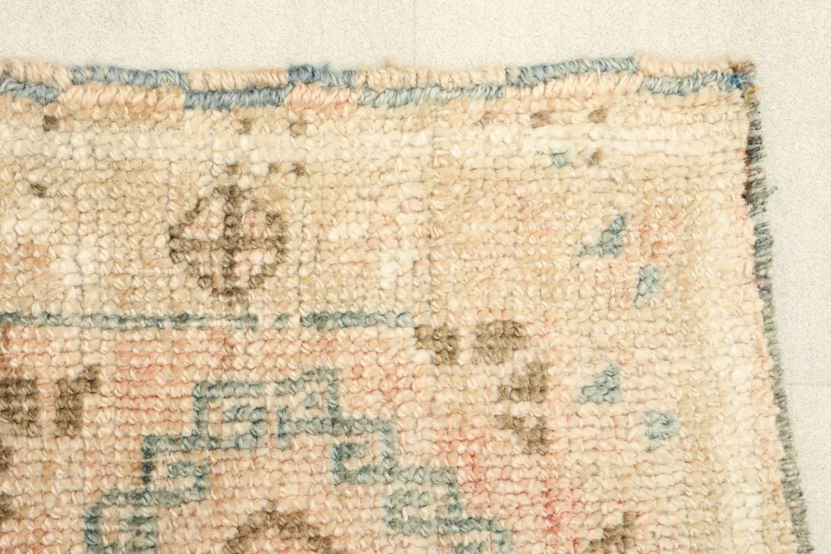 Close-up of the rug's edge and a section of the geometric pattern in beige, rose, and brown.