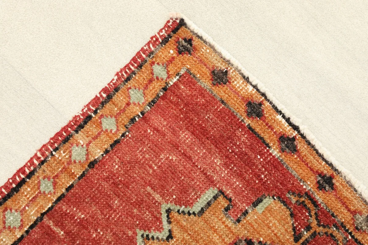 Corner view showing the orange border with small geometric motifs and the short, natural fringe.