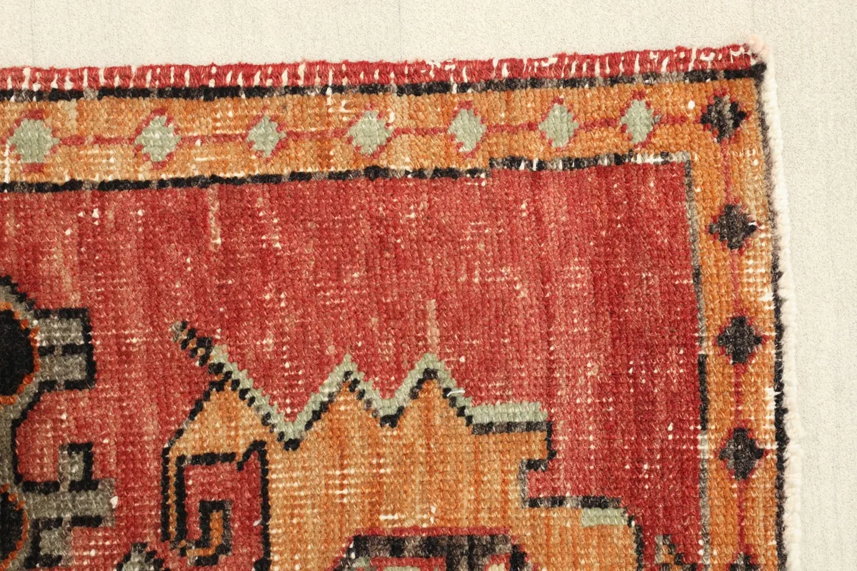 Edge view of the rug, highlighting the orange and black border design and the texture of the wool pile.
