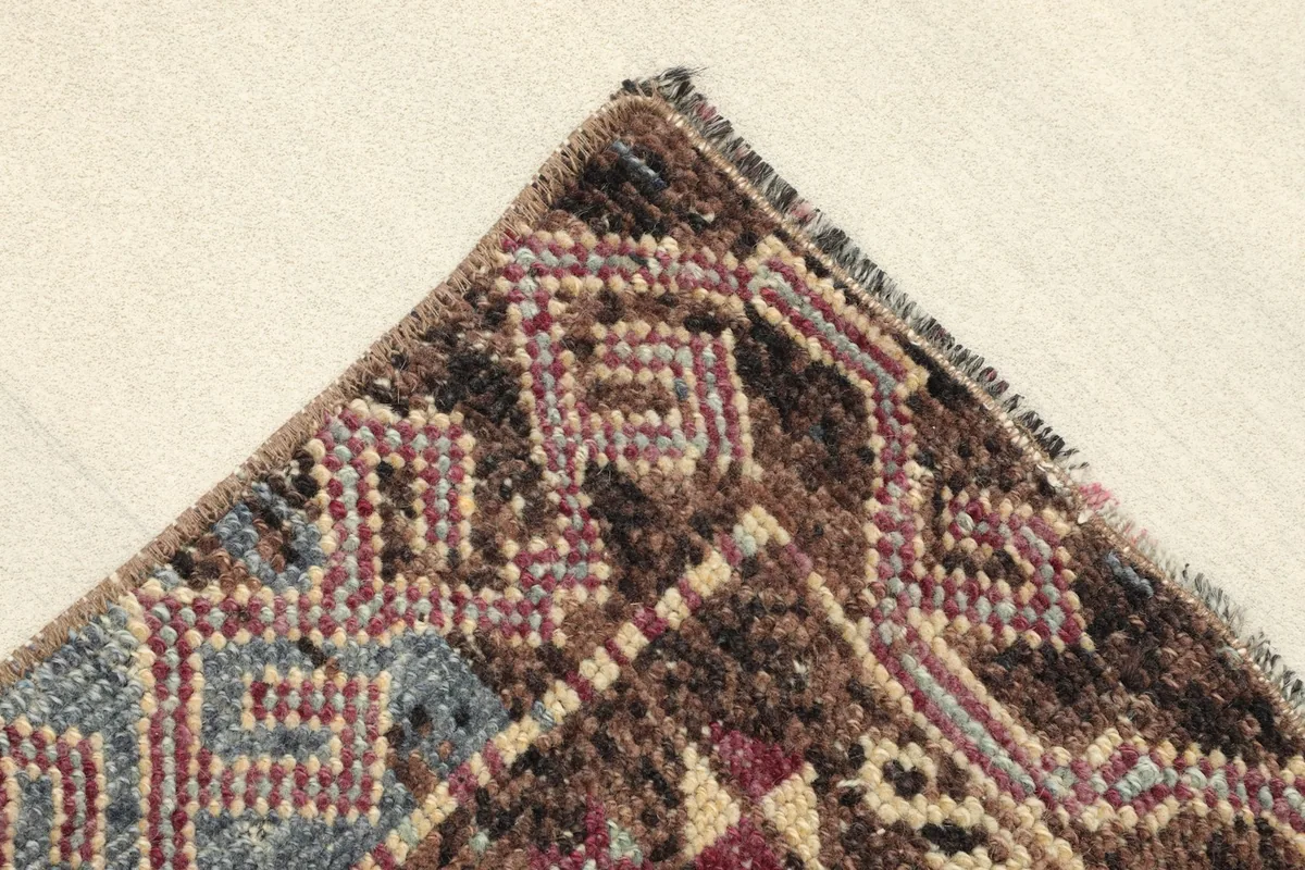 Corner detail showing the brown and blue geometric border pattern and the edge finishing of the rug.