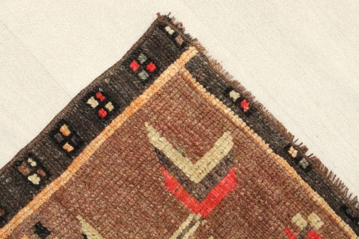 Corner detail showing the dark brown border with small multicolor square patterns and fringe.