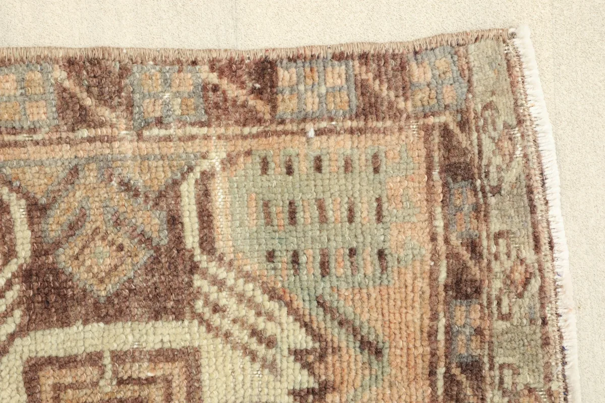 Close-up of the rug's border with brown and olive geometric motifs and slight wear.