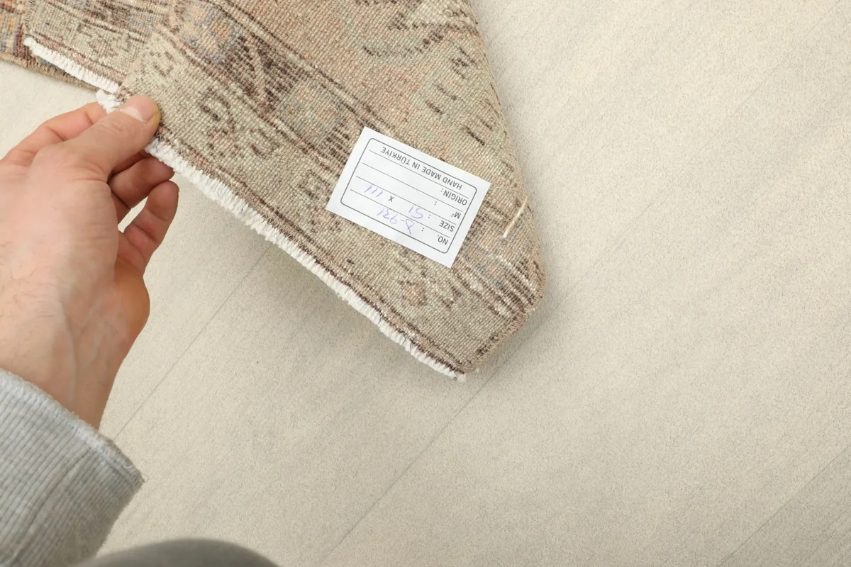Hand holding a corner of the rug, displaying the label and the quality of the hand-knotted back.