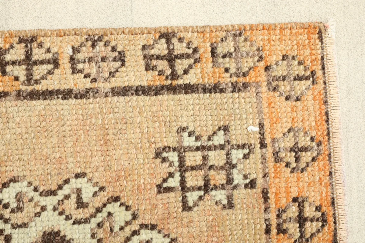 Close-up of the rug's corner, showing the distinct orange border and a beige field motif.