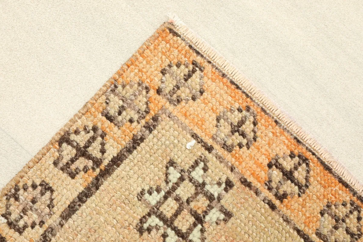 Corner detail showing the orange border with tribal elements and the beige field.