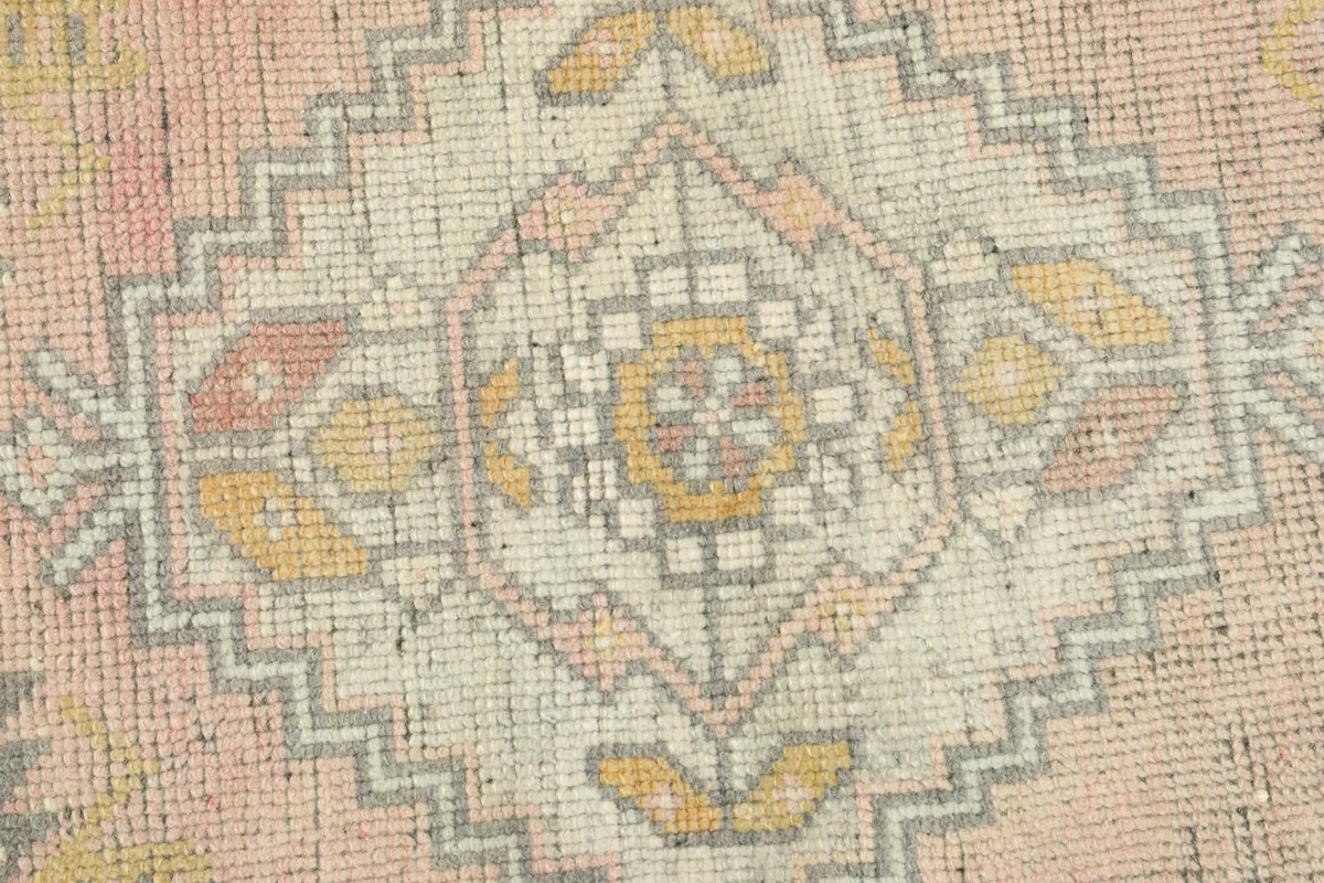 Detailed close-up of the central geometric medallion with pink, gold, cream, and gray threads.