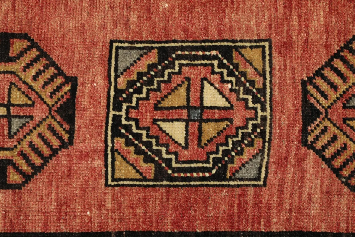 Detailed view of a central geometric motif in black, tan, rose, and gray on the rug's rose field.
