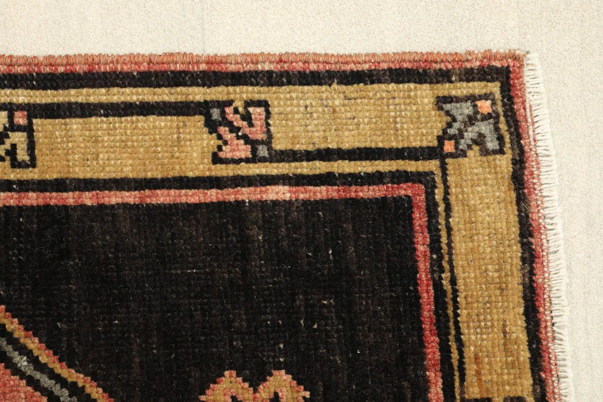Edge detail of the rug's border, highlighting the tan, black, and rose colors and minor wear.