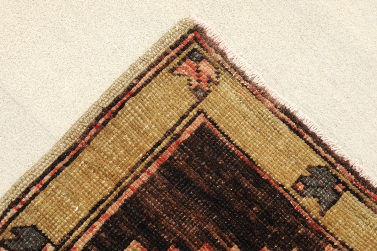 Corner detail showing the brown and tan border with small geometric accents and faded rose field.