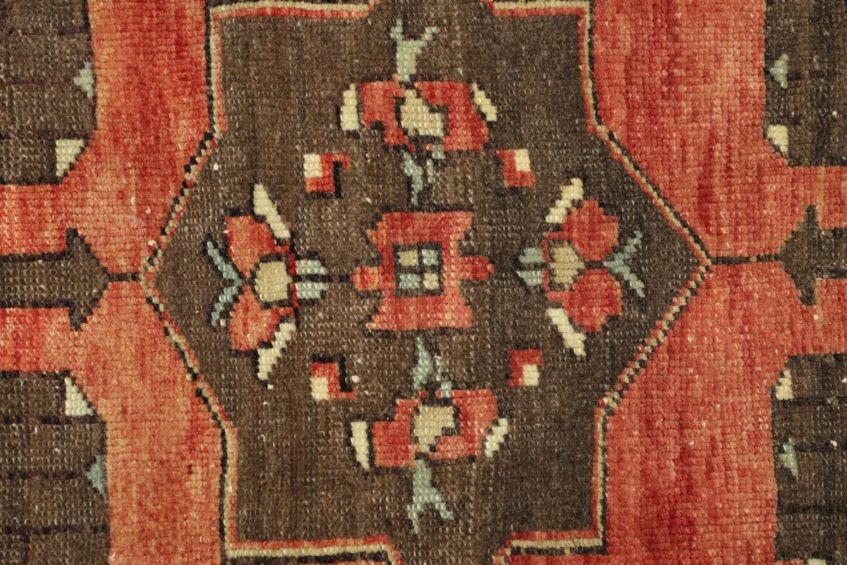 Close-up detail of the central brown geometric motif with red, green, and beige accents.
