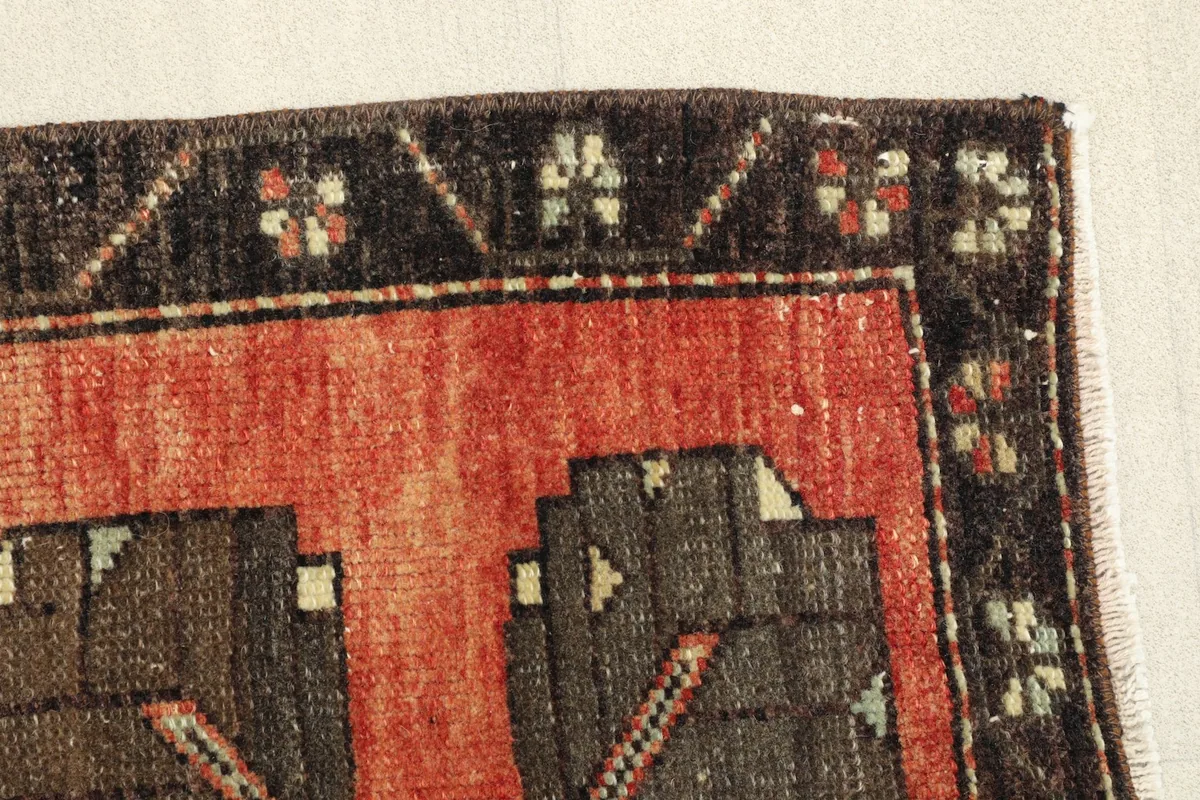 Close-up of the rug's edge, revealing the black border pattern and the rust field with low pile.