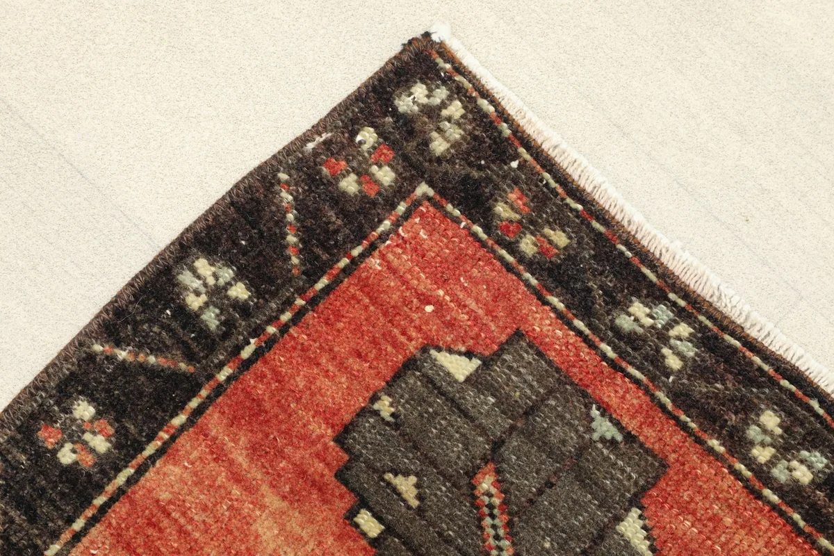 Detail of the corner, showing the black border with small floral-like motifs and the rust field.
