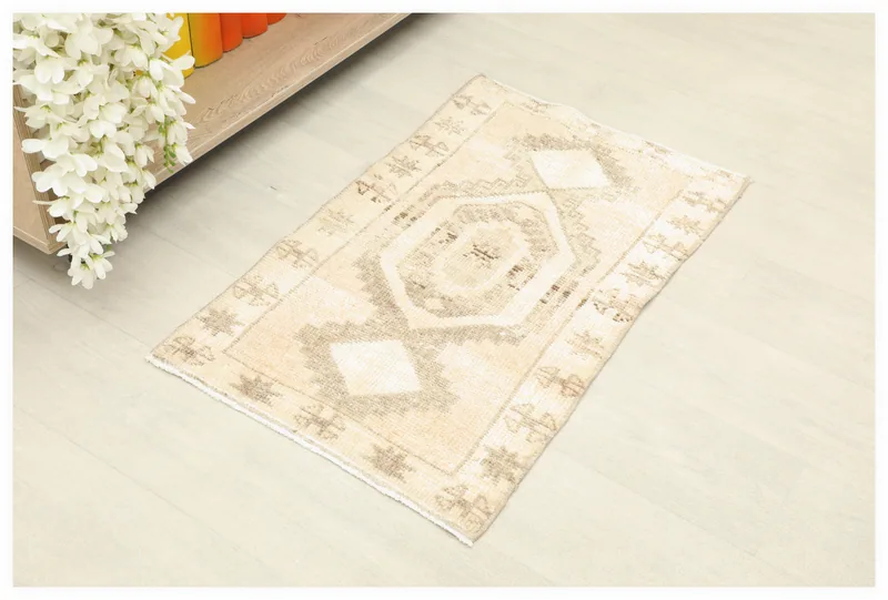 Full top view of the beige geometric doormat rug on a light floor, with flowers in the corner.