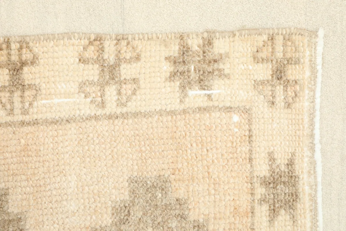 Detail of the rug's border, featuring a row of small tribal motifs in tan and brown on a cream background.