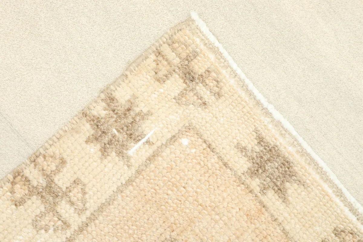 Close-up of a corner of the rug, showing the beige field, tribal border motifs, and fringe.
