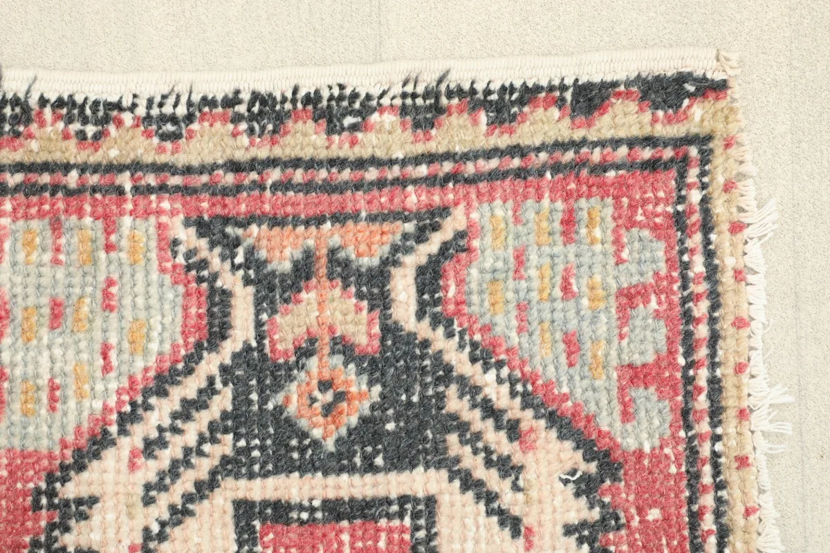 Close-up of the rug's border, showcasing the red, black, and beige colors and hand-knotted texture.