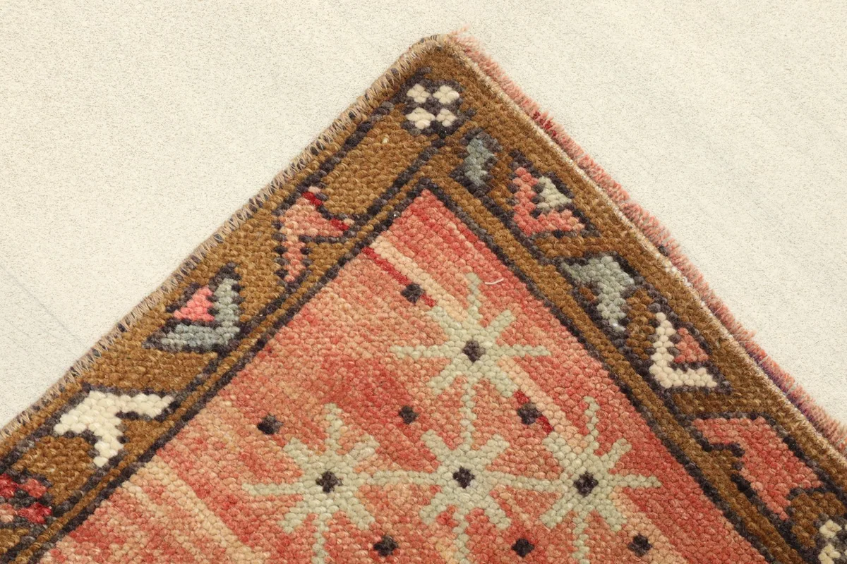 Corner detail of the rug, showing the brown border and star-like motifs on the rust field.