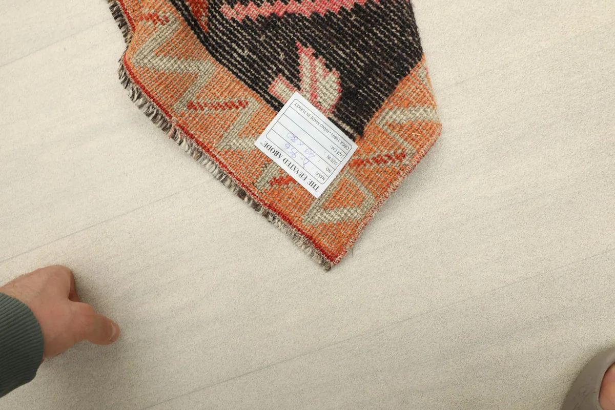 A hand next to the rug's corner, indicating the small scale and size of the doormat.