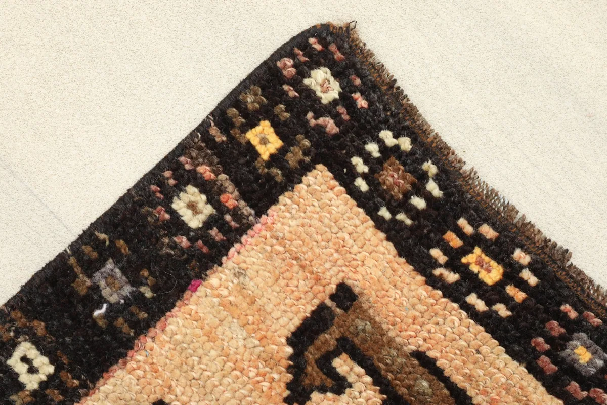 Corner detail showing the dark brown border with small colorful squares and the beige field.