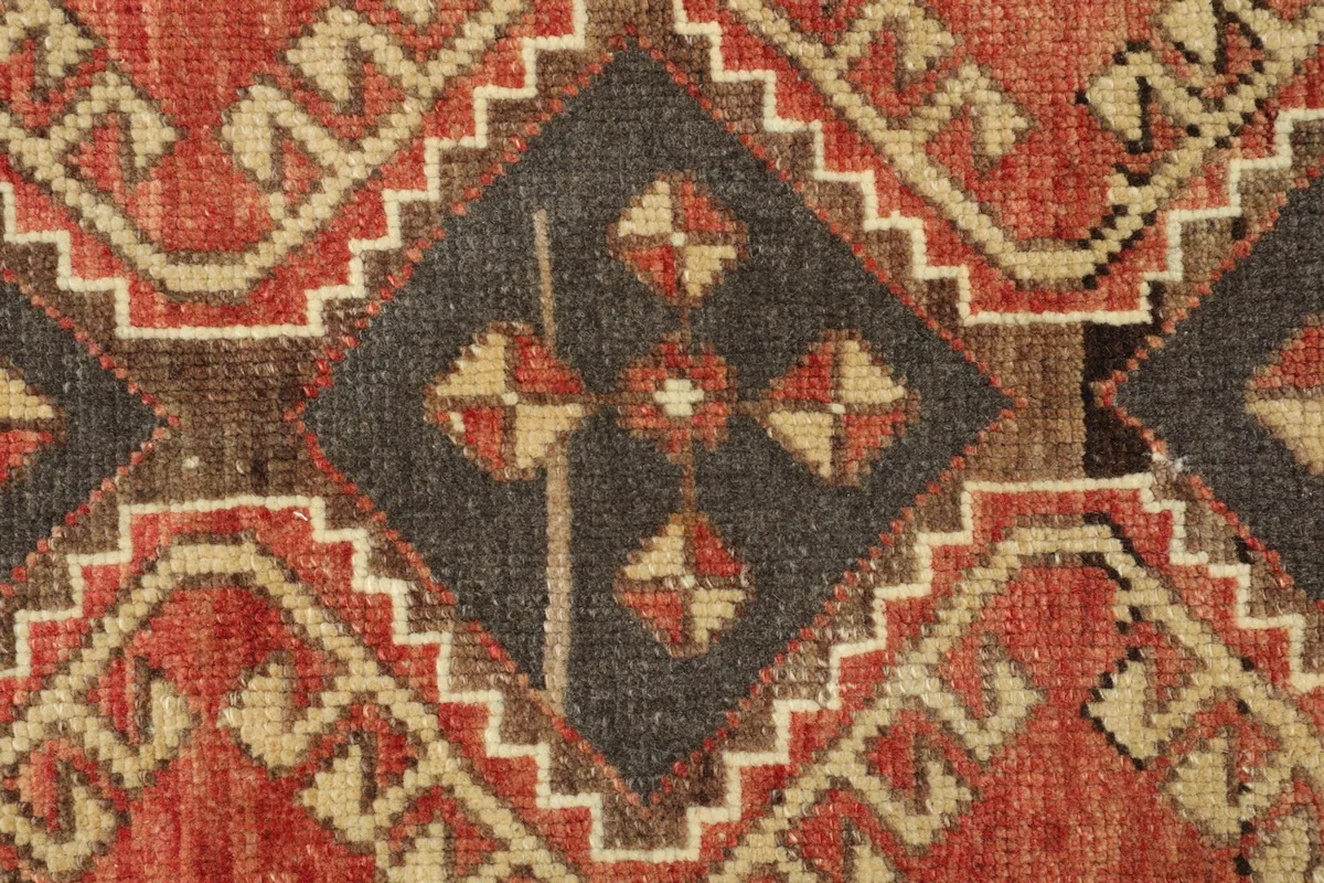 Close-up detail of the central charcoal geometric motif and surrounding rust and beige patterns.