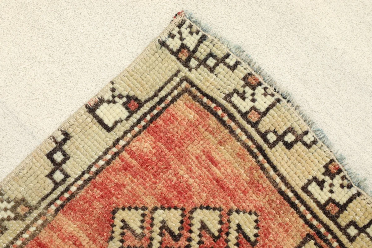Corner detail showing the beige border and the edge of the rust field with minor fringe.