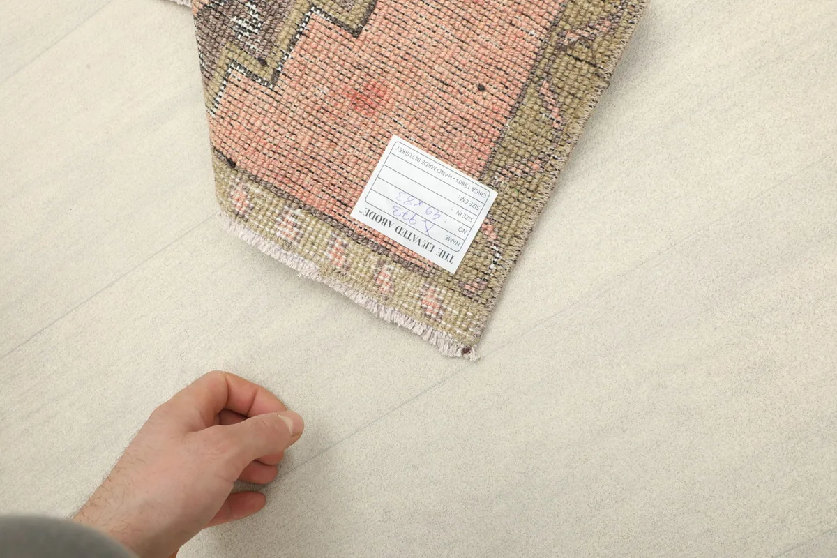 Hand pointing to the label on the back of the rug, showing its hand-knotted cotton foundation.