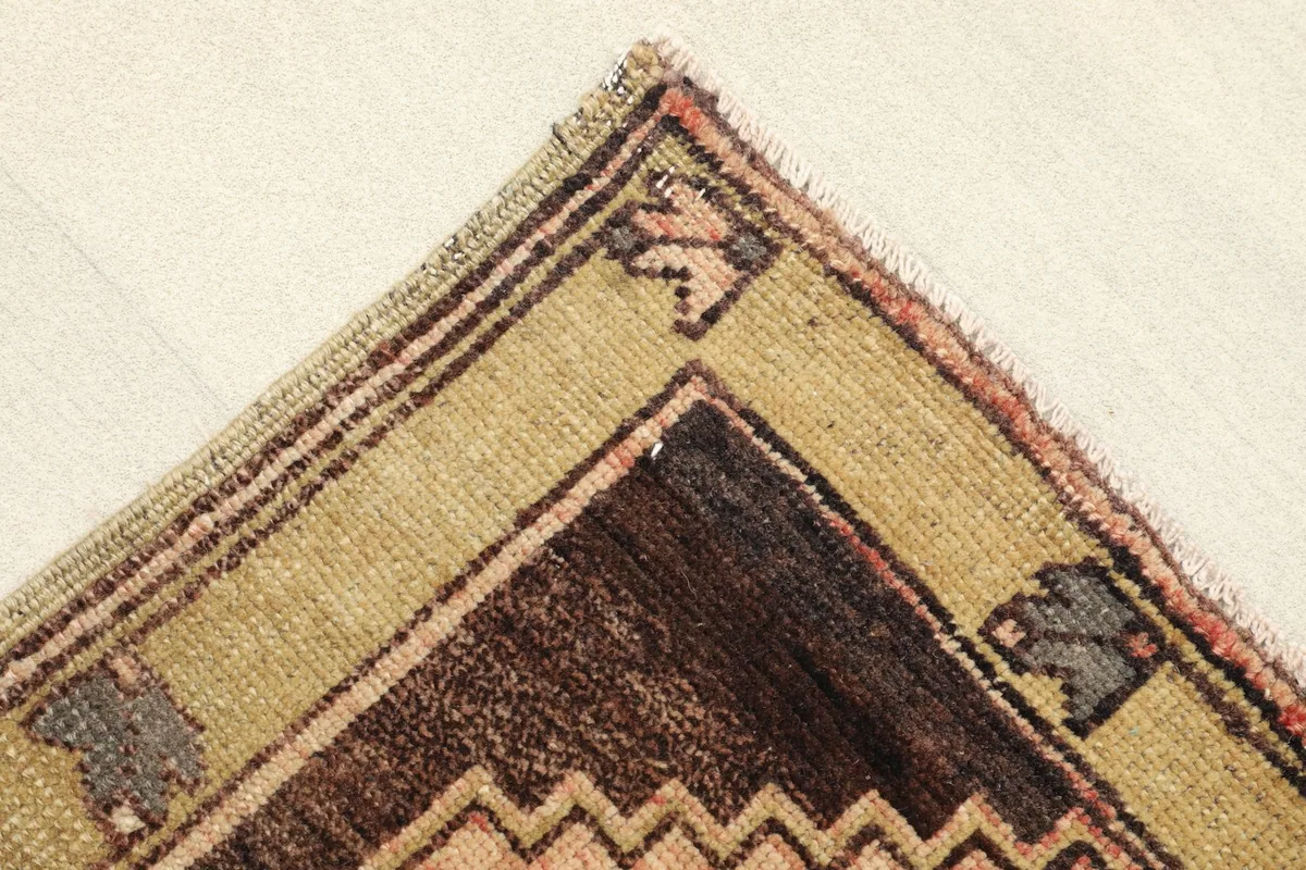 Close-up of the corner, revealing the olive border and brown geometric patterns of the vintage rug