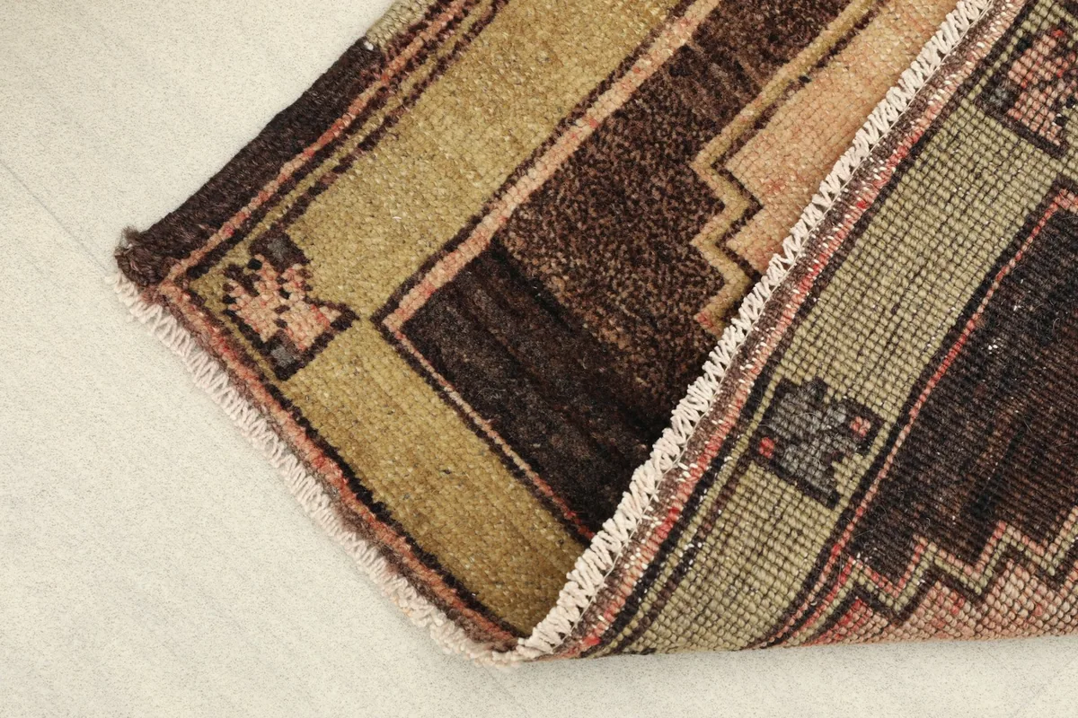 Side view showing the low pile and texture of the hand-knotted wool rug, with a corner folded