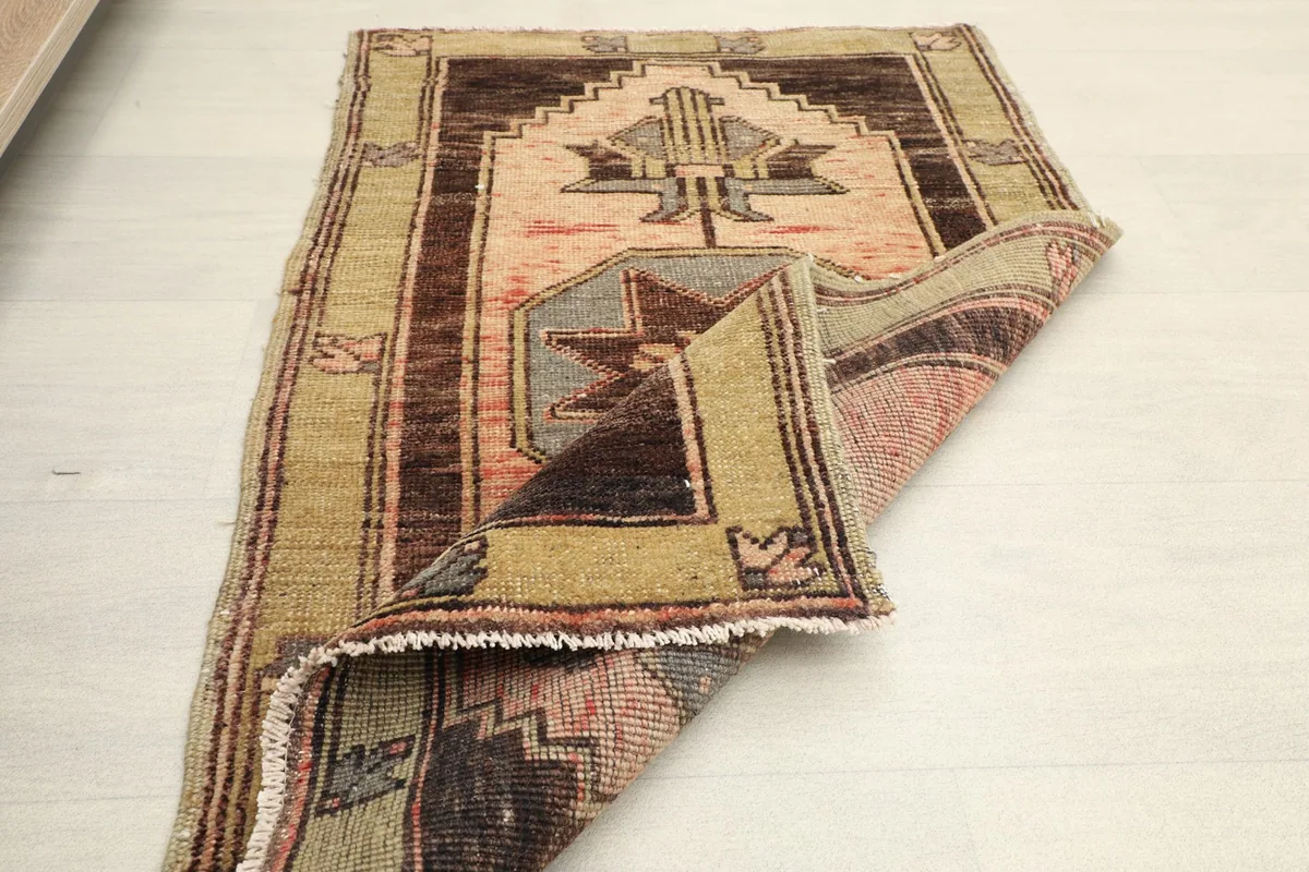 The small area rug partially folded, displaying the back and the blend of rose, brown, and olive colors