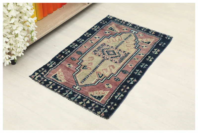 Full overhead view of the rose and navy hand-knotted vintage Anatolian doormat on a white background.