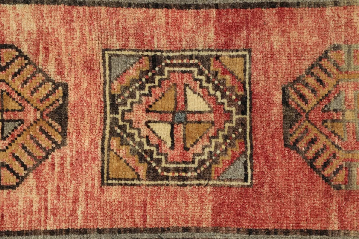 Detailed view of the hand-knotted geometric motifs and the texture of the rose wool pile.