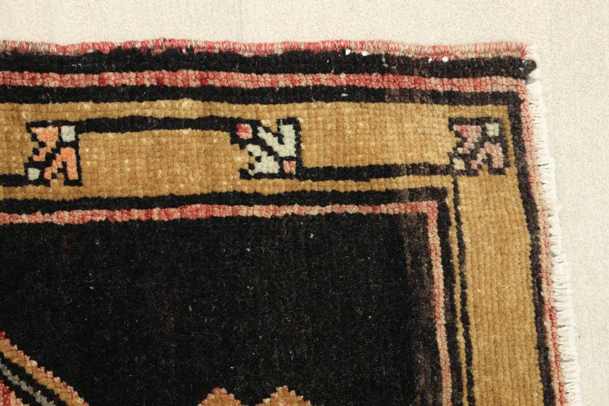 Edge detail of the rug's border, highlighting the gold and black framing and small geometric elements.