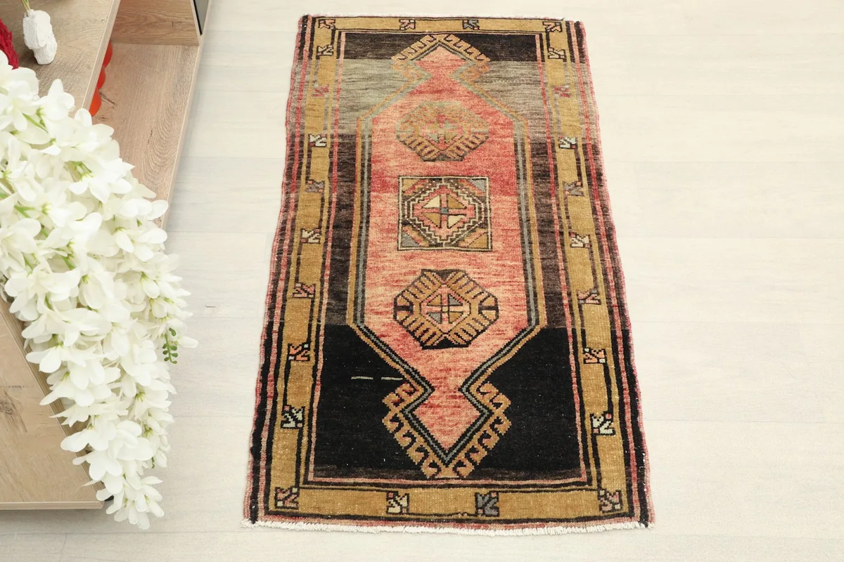 Overhead view of the vintage Anatolian doormat, showing its rose field and black and gold geometric patterns.