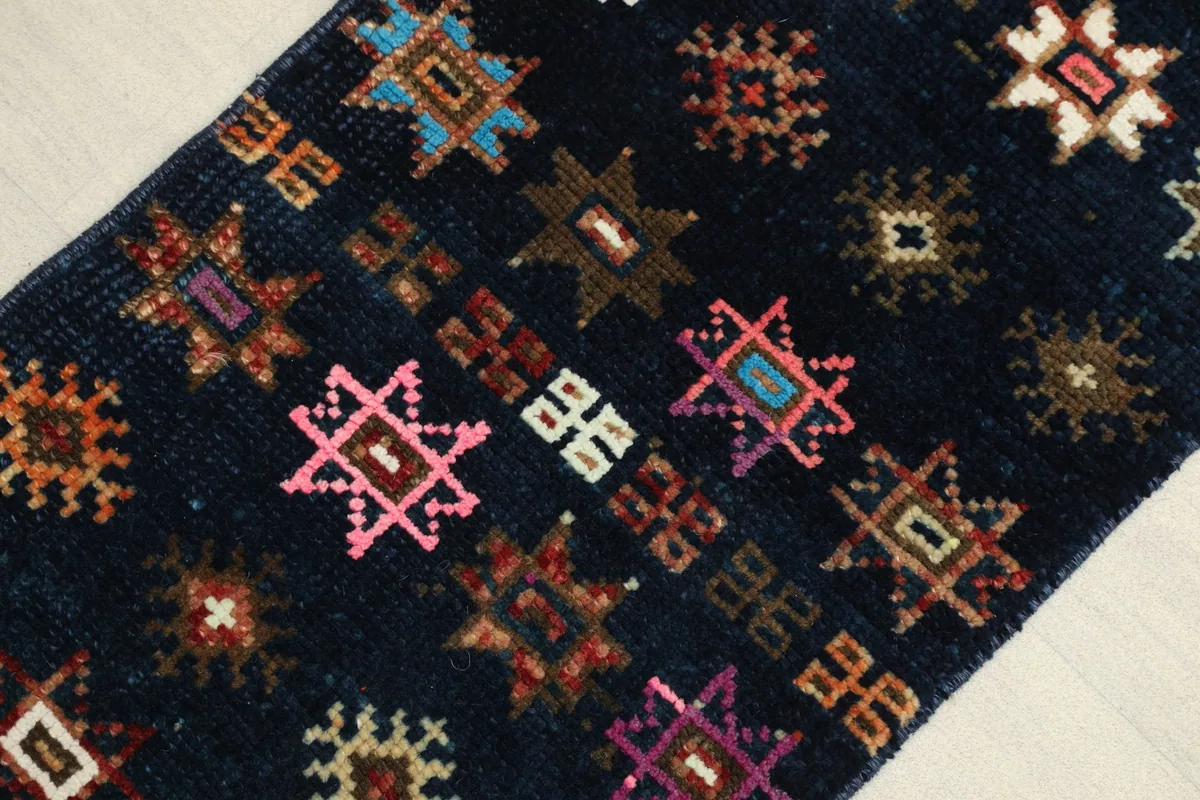 Close-up detail of the hand-knotted wool pile showing rose, pink, and blue geometric motifs on navy.