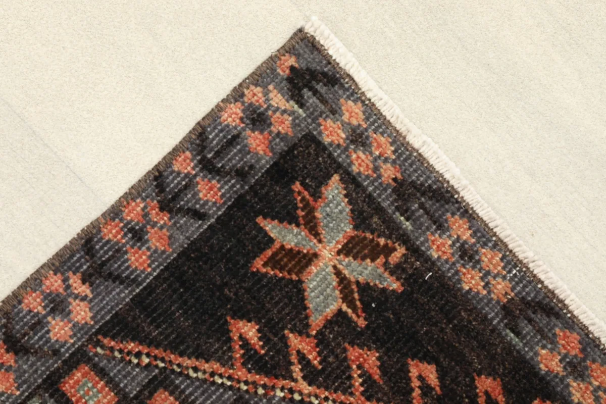 Corner detail of the rug, highlighting the charcoal border with rust and gray star-like tribal elements.