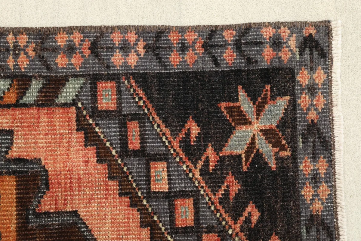 Edge detail of the rug, showing the geometric border patterns and the subtle color fading of the vintage wool.