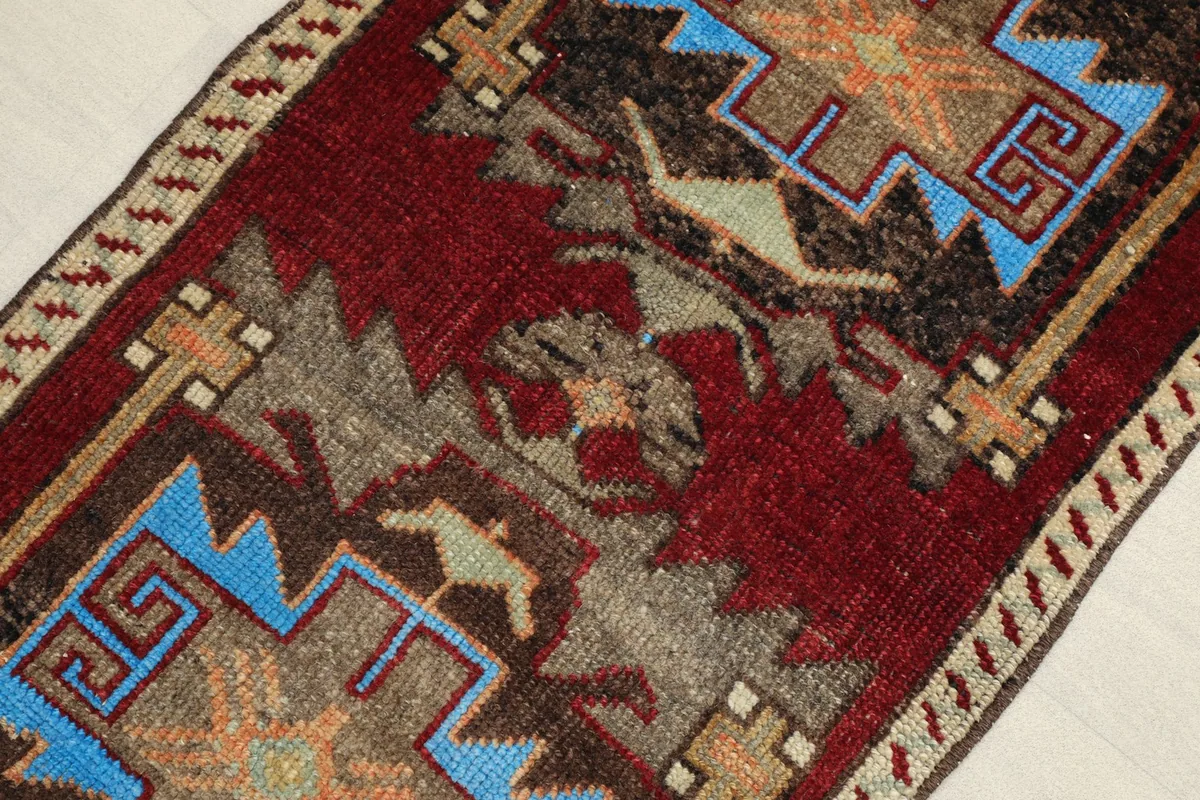 Angled view highlighting the deep red field and intricate geometric motifs, showing texture and color variation.
