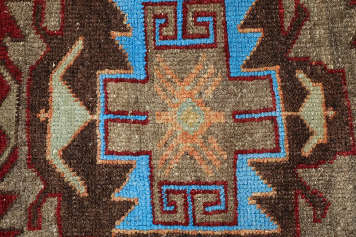 Close-up detail of a central geometric motif in blue, brown, and orange, revealing knotting and wool fibers.