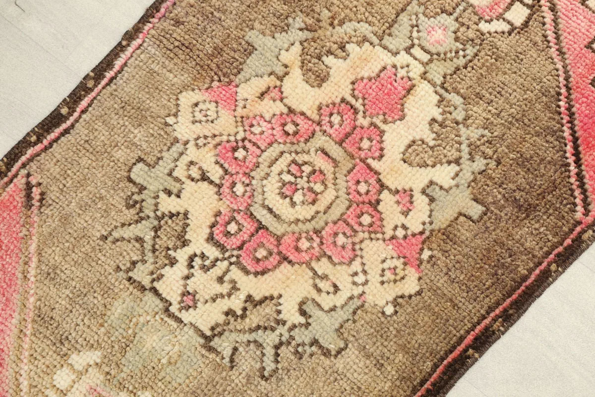 Angled view highlighting the pink and ivory medallion motif on the brown wool rug