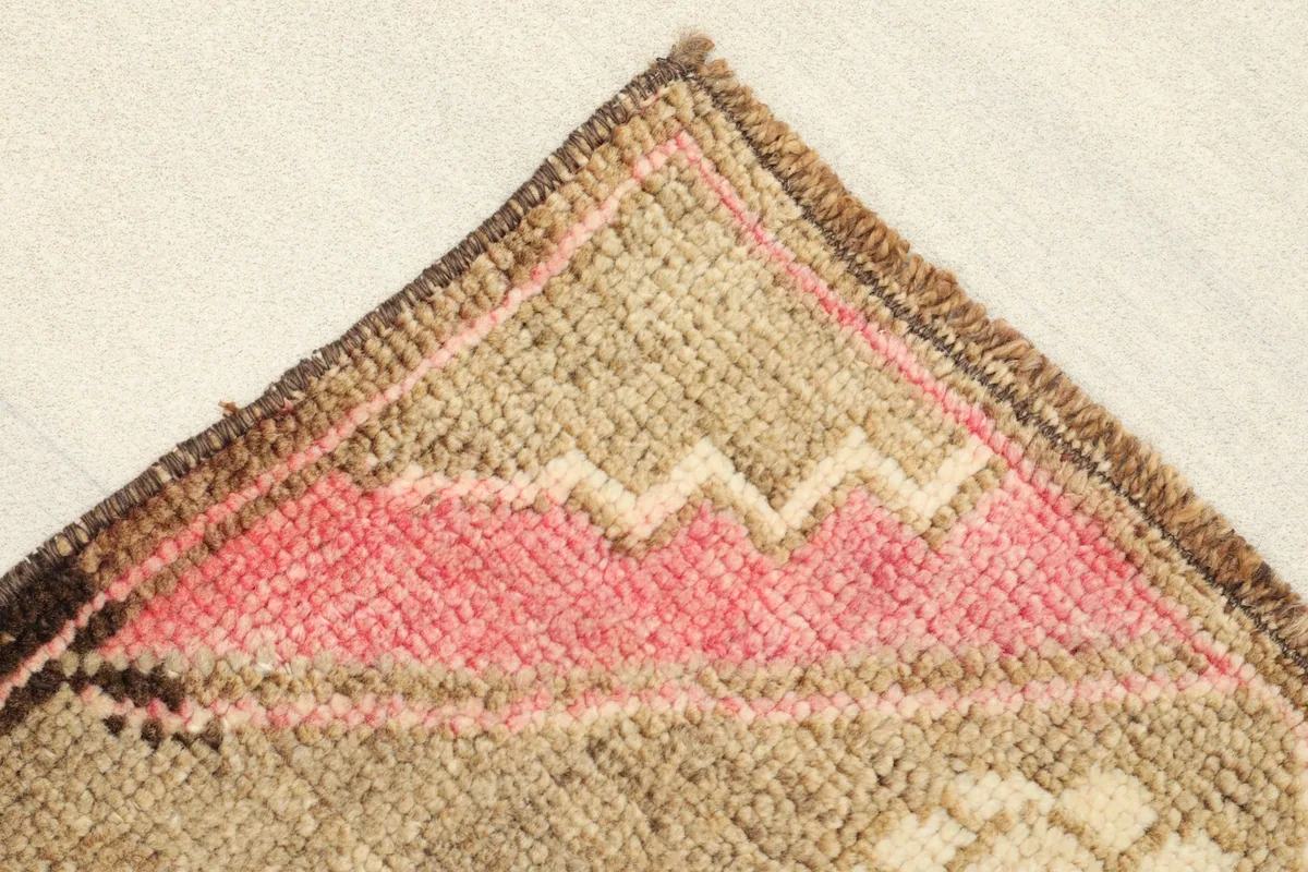 Detailed view of the corner with geometric pink and ivory patterns and brown border